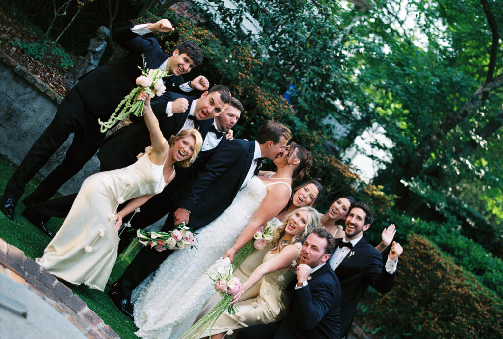 Film photo of a couple kissing with their bridal party cheering around them.